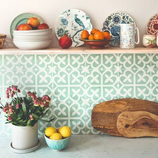 A kitchen with a tiled, patterned backsplash, wooden chopping boards and bowls of fruit