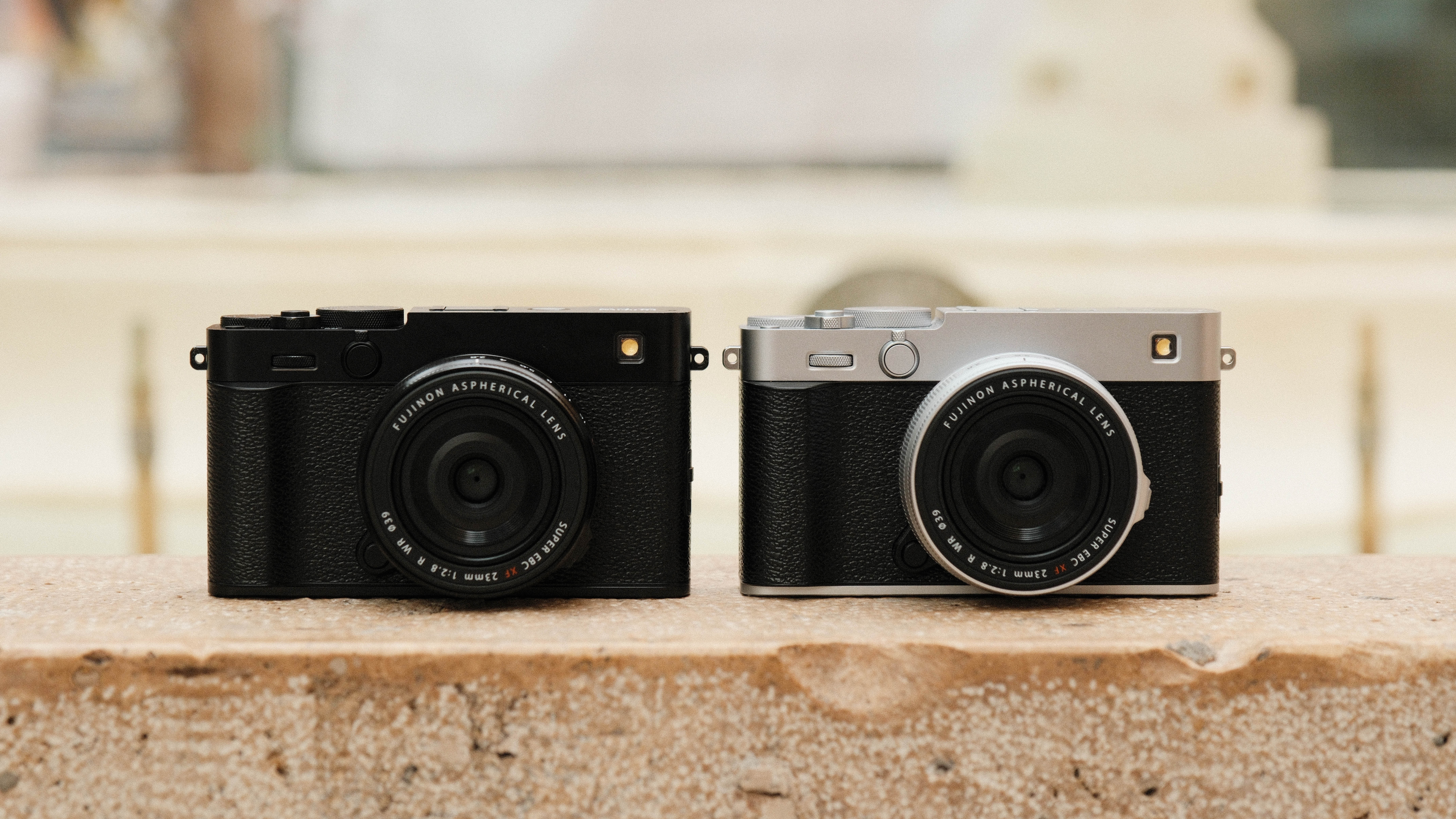 Two Fujifilm X-E5 cameras in black and silver next to one another on a stone wall