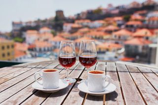 Two glasses of Madeira wine and two cups of coffee on a table overlooking the city of Funchal, Madeira