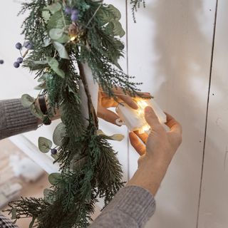 A DIY space-saving Christmas tree being wrapped in battery operated string lights