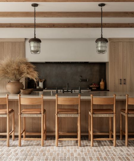 A wooden kitchen with shiplap-style cabinets, a black metal backsplash and brick floors