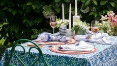 table set out in the garden with blue and white tablecloth, tall white candles, vases of flowers and glasses of wine