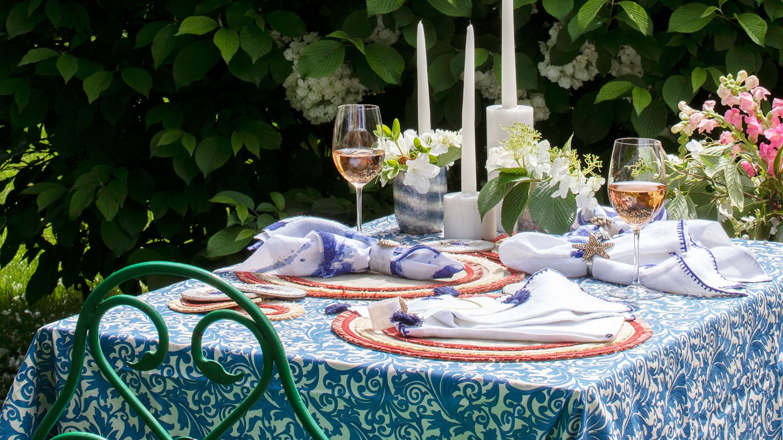 table set out in the garden with blue and white tablecloth, tall white candles, vases of flowers and glasses of wine