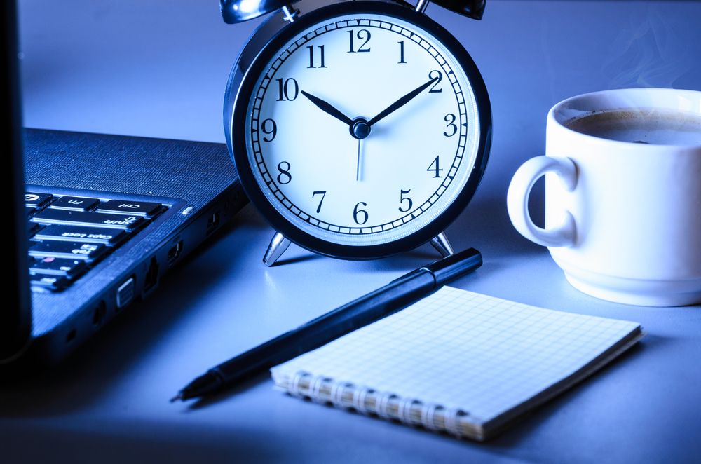 Alarm clock, notebook, laptop and coffee with a blue filter