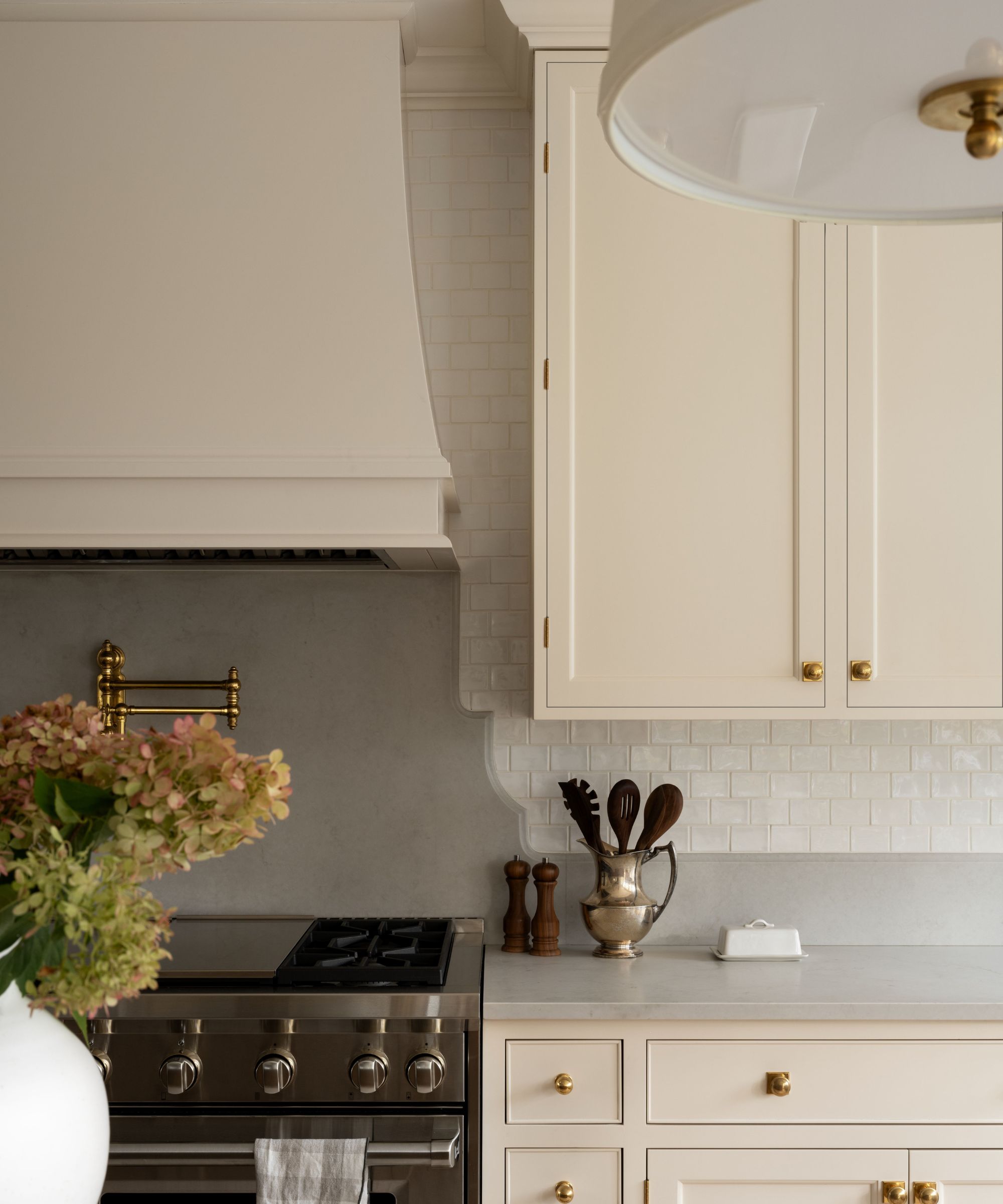 A kitchen with warm white cabinets and a curved edge backsplash in a gray stone
