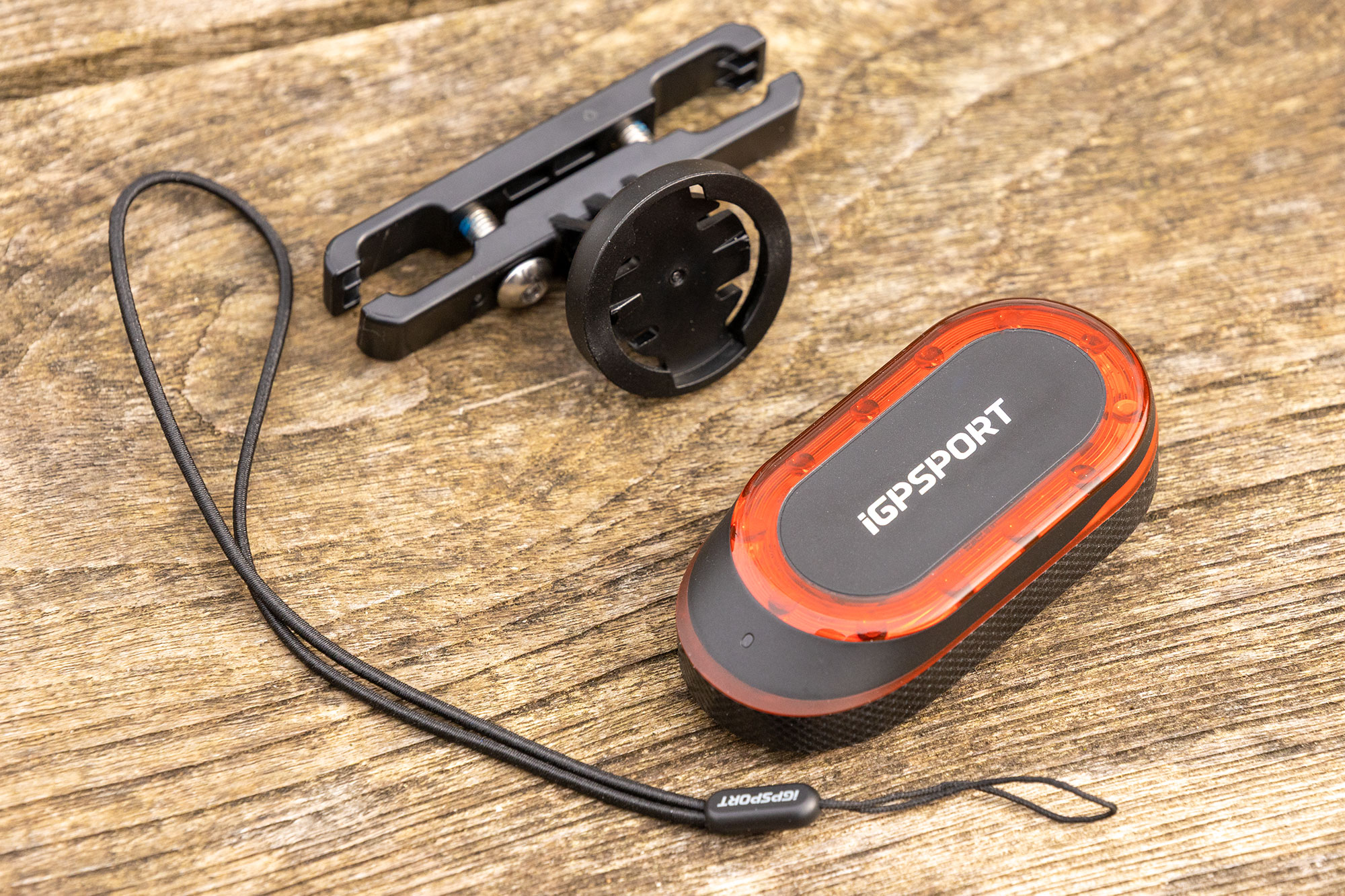 iGPSport SR Mini pictured off-bike, on wooden table with saddle rail mount and lanyard