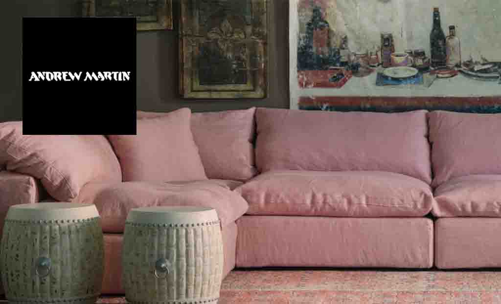 andrew martin logo top left corner of the image with a pink l shaped sofa and large paintings behind it