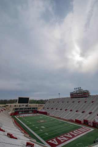 A cloudy sky hangs over a football stadium, seen wide, with reaching stands and an empty painted field.