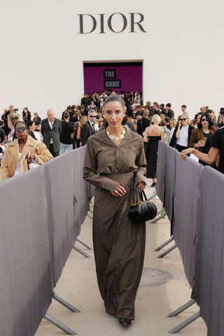Bettina Looney at Dior Paris Fashion Week walking towards the camera with a black Dior handbag