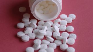 small round white tablets spilling out of a jar onto a pink background