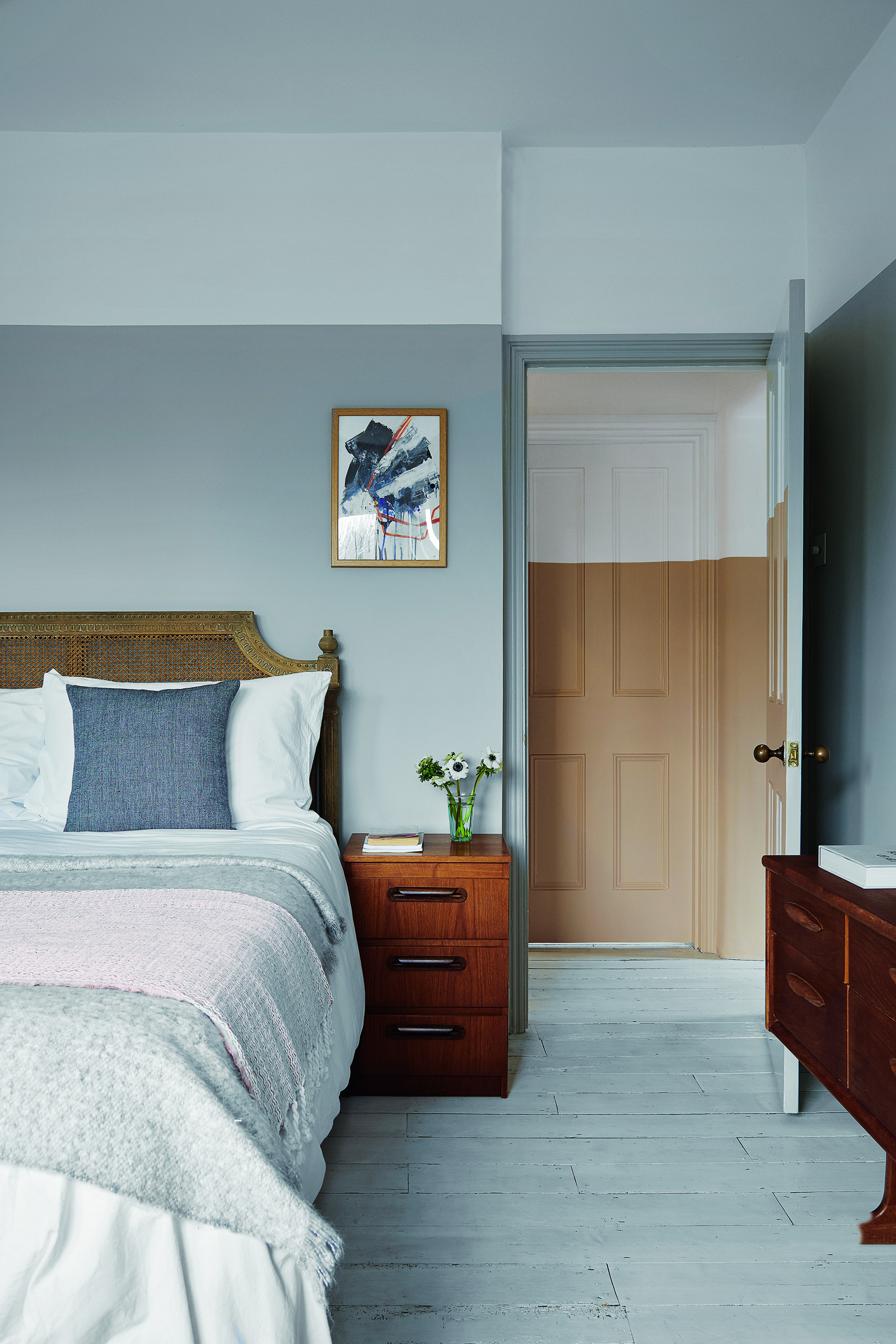 Bedroom with white painted wooden floor and view through open painted doorway to the landing.