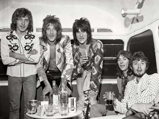 The Faces in 1971: L-R: Kenney Jones, Rod Stewart, Ronnie Wood, Ian McLagan, Ronnie Lane, posed, with drinks, at press call on top deck of bus