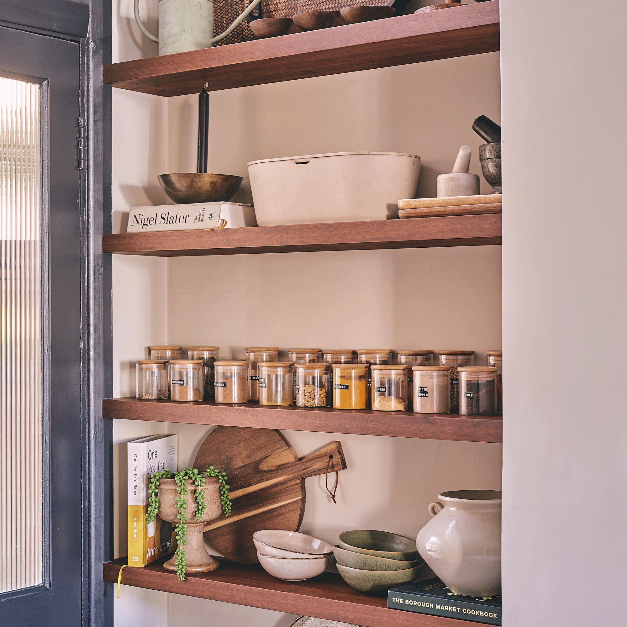 a kitchen with open alcove shelving with matching decanted spice jars and kitchen accessories