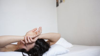 Woman lying face up on bed with hands resting on her forehead