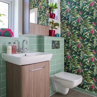 Bathroom with green wall tiles and brightly patterned leaf wallpaper