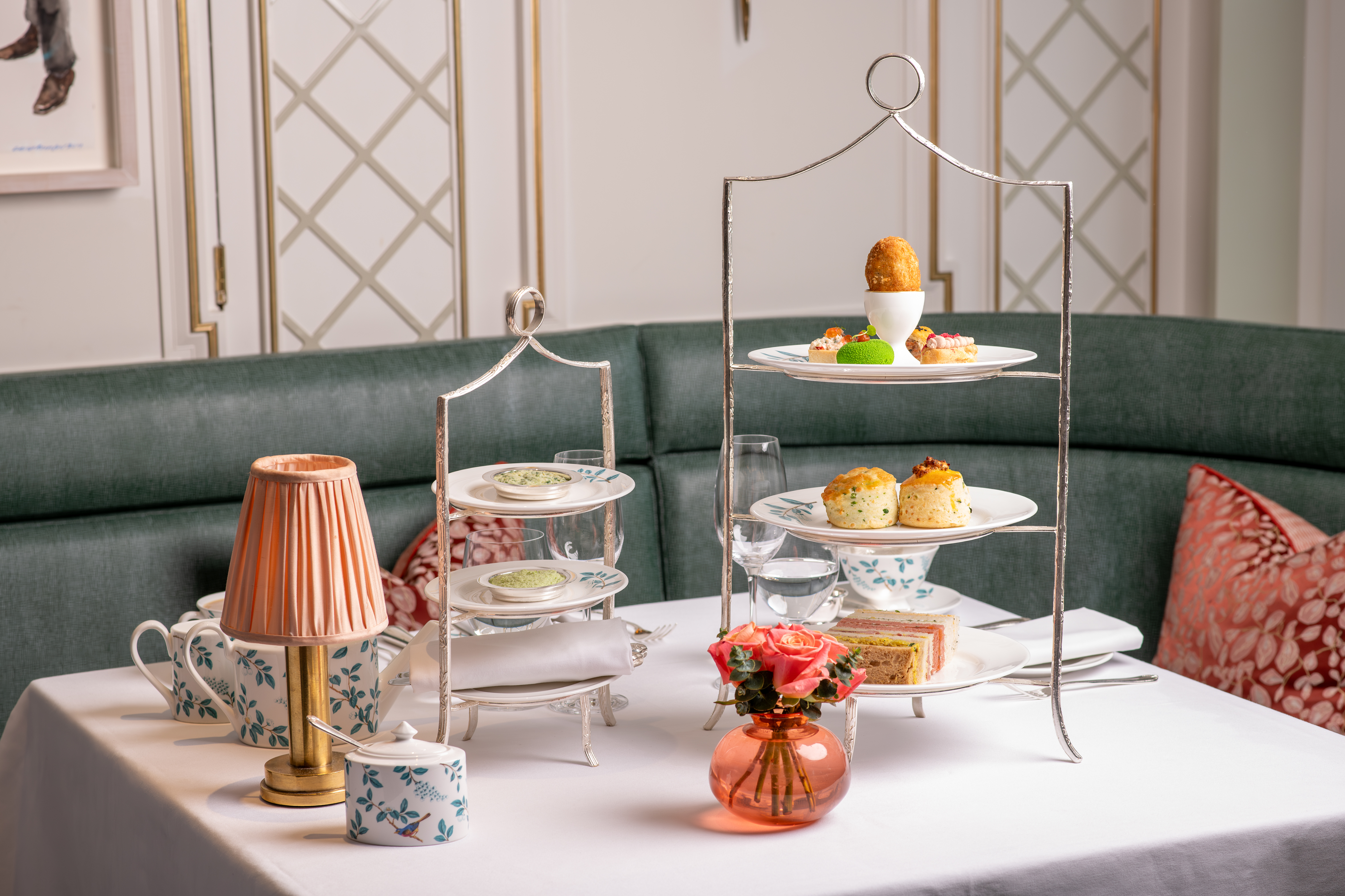 An Art Deco-infused tea room with plush, teal seating, spirited artwork, golden lighting, and textural table lamps.