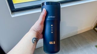 A hand holding the Ember Travel Mug 2+ with the LED display lid