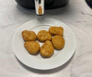 Chicken nuggets on a plate in front of the Prosenic T22 air fryer.
