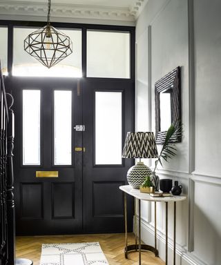 Hallway with large pendant light and console with table lamp and mirror above, wood floor and runner