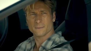 Glen Powell looking wistful staring out a car window wearing earrings in Chad Powers trailer.