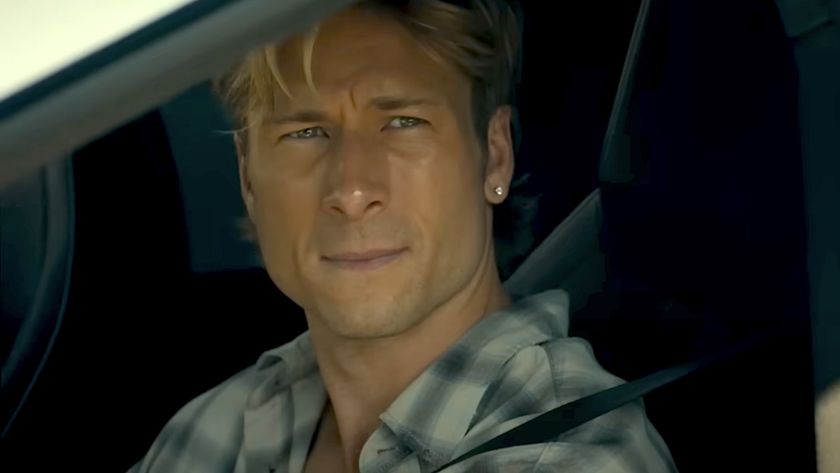 Glen Powell looking wistful staring out a car window wearing earrings in Chad Powers trailer. 