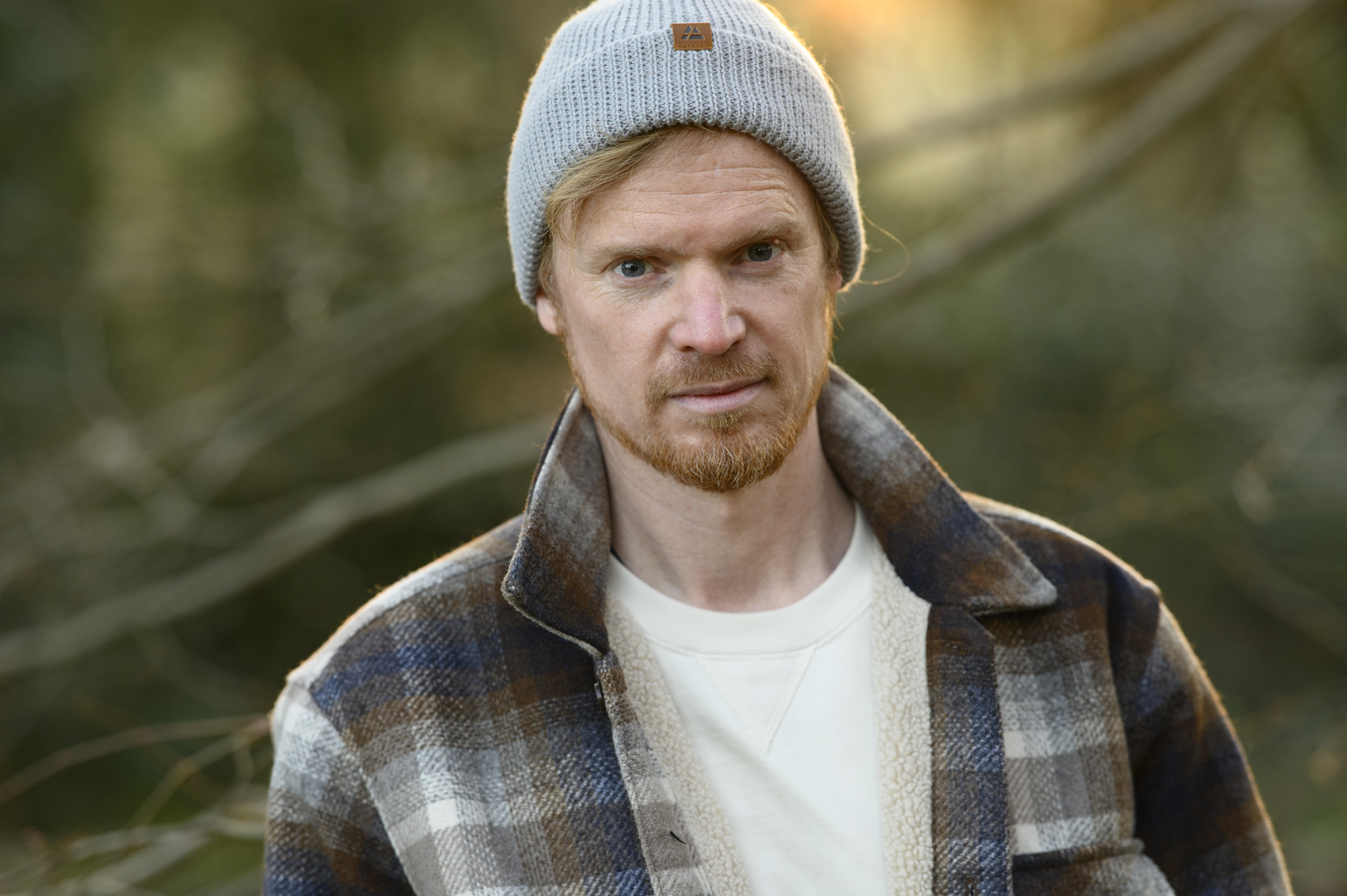 Portraits of a man in a beanie hat and shacket and golden hour with dappled light in background