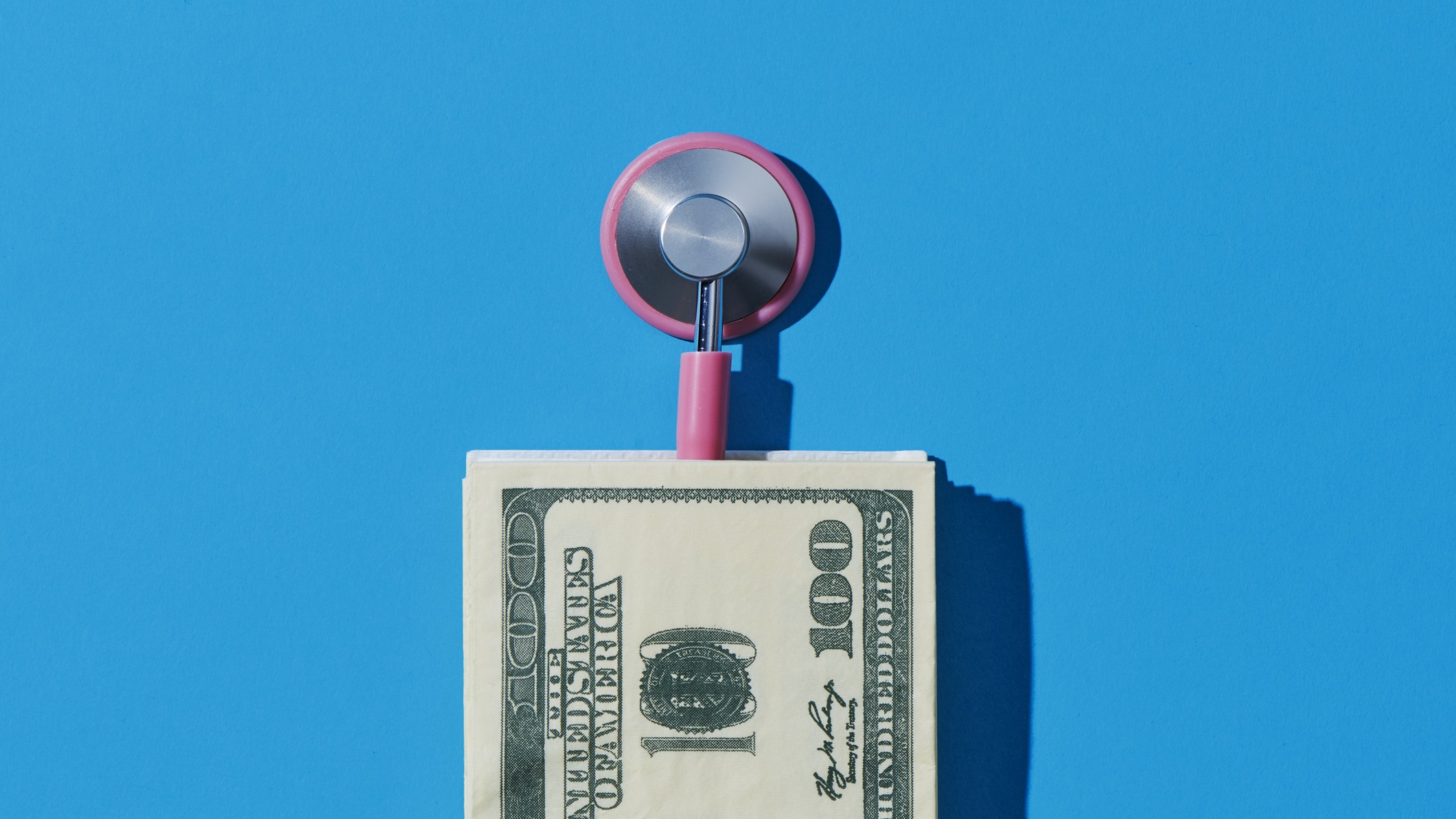 closeup of a pink stethoscope and a pile of fake US dollars, on a blue background