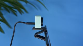 a photograph of a 1 inch wide mint webcam with a 4K sensor and built-in microphone, photographed against a blue background