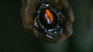 The Curse of the Necklace's cursed jewelry, being held in a dirty hand in dim lighting.