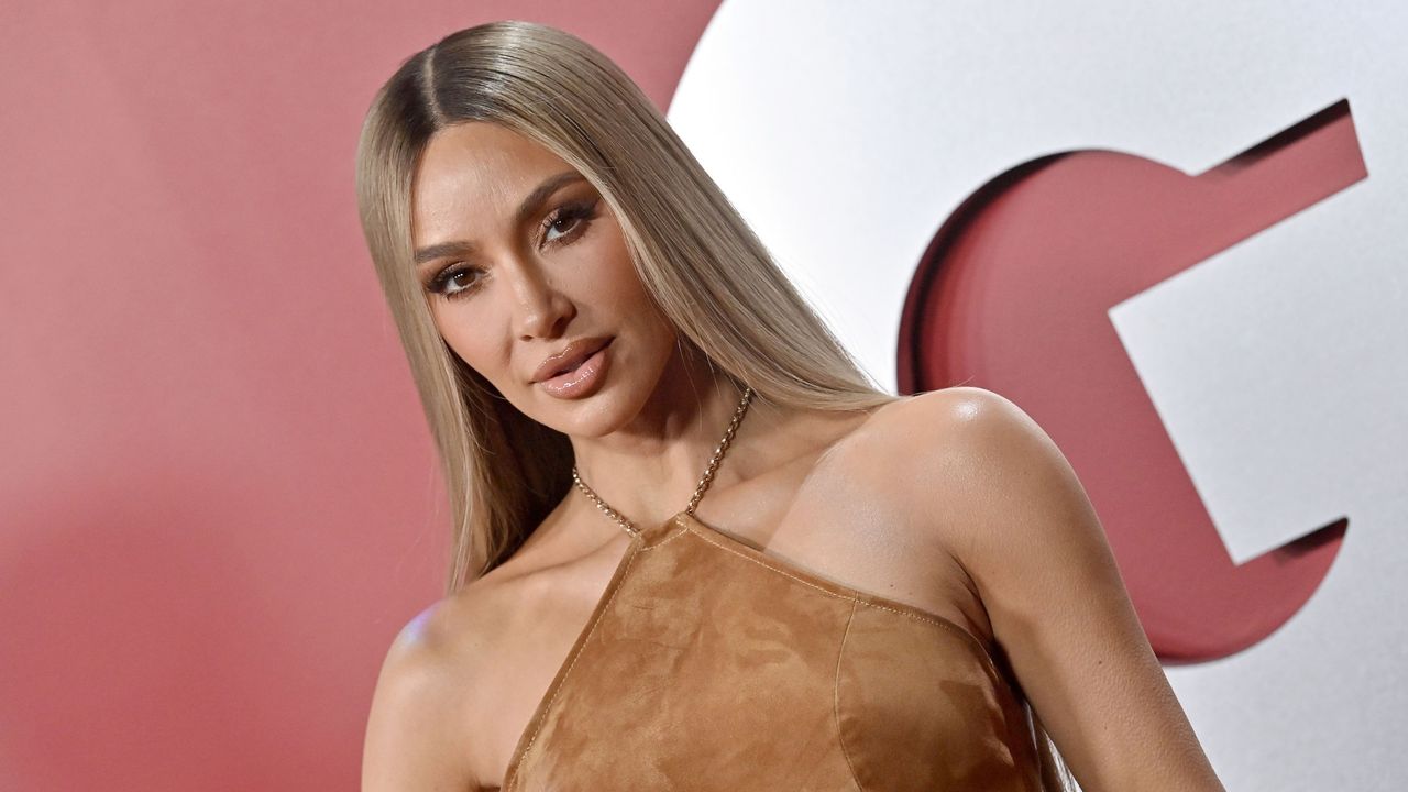 Kim Kardashian in a brown dress against a red background