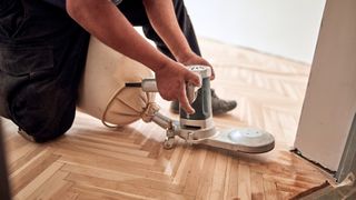 Man using a handheld sander to restore herringbone hardwood floors