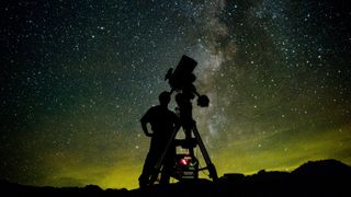 An astrophotographer with a telescope in front of the Milky Way.