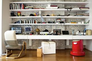 Wall to wall desk with white shelves on brick wall