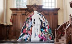 Inside Blenheim Palace looking at a white naked statue with its back to the photographer. In front of the statue is a pile of clothes at the same height as the statue. 