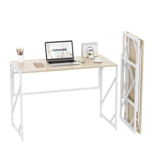 A light brown wooden desk with white metal legs with a laptop, photo frame, and pencil pot on it, with a folded version of it next to it