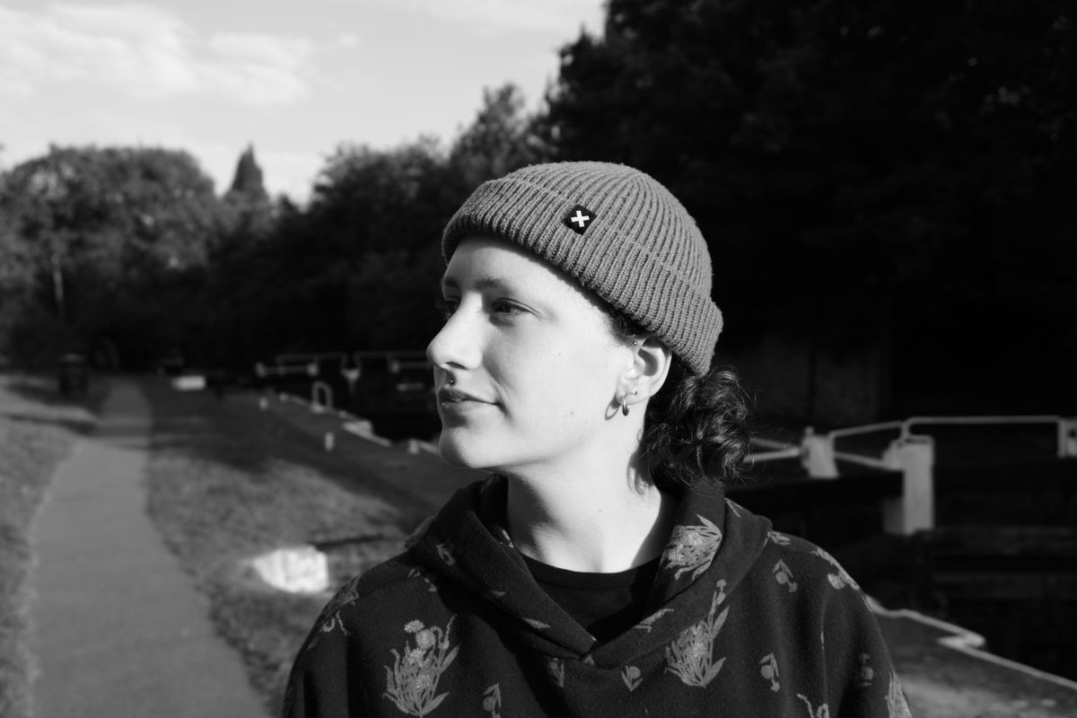 A photo of a woman with curly hair, wearing a hoodie and a beanie, taken on a Sony ZV-E10 II vlogging camera
