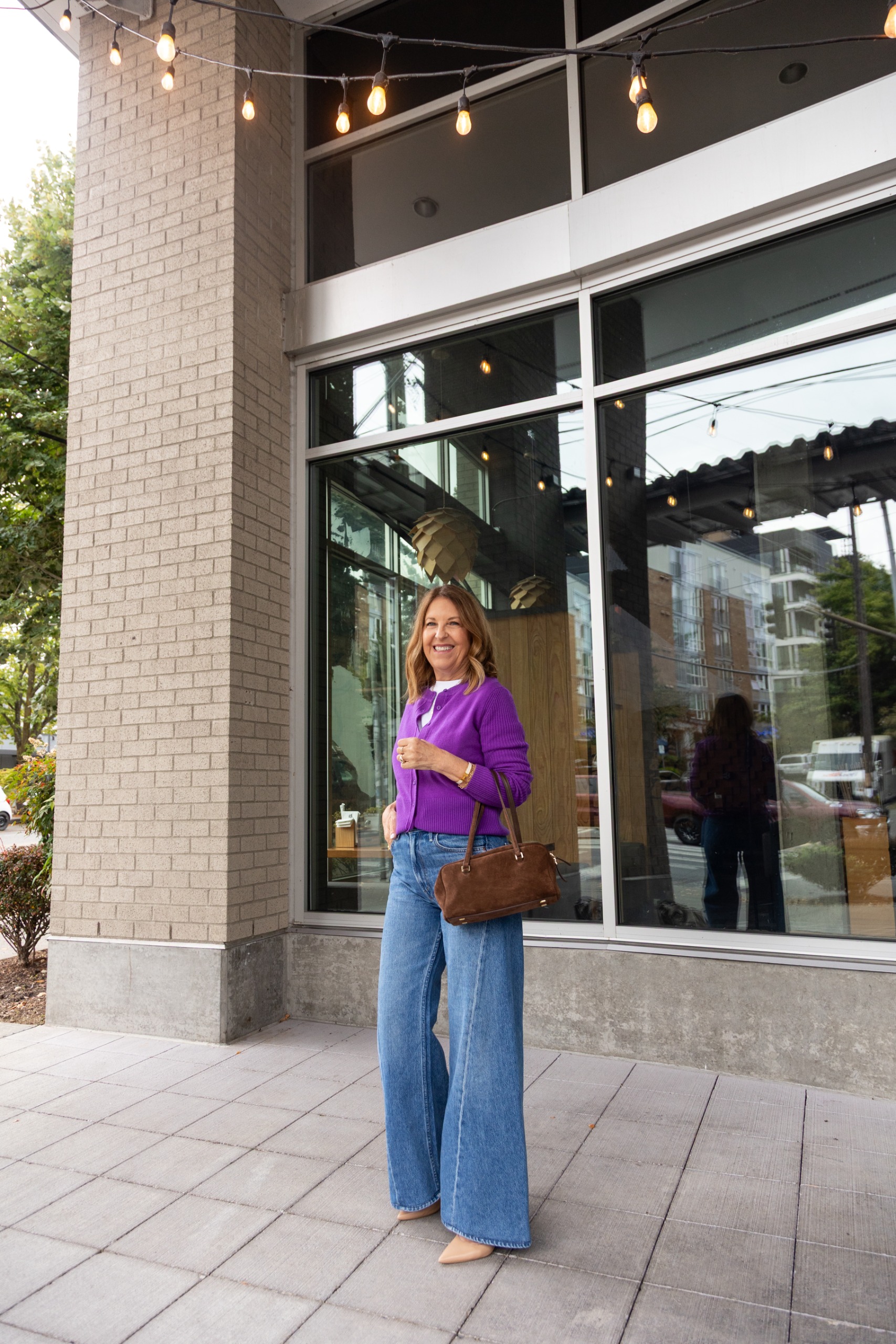 Sandy Koszarek wearing a purple cardigan, white tee, and jeans.