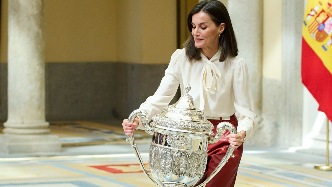 Queen Letizia of Spain lifts a trophy while wearing a white blouse and red leather pants