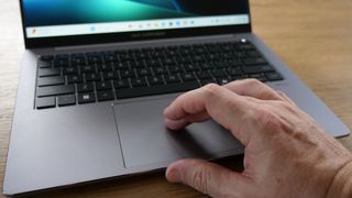 Asus ExpertBook P5 (P5405) open on a wooden table with a hand scrolling on the touchpad