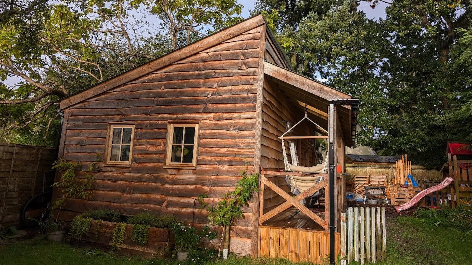 A wooden shed with a porch with two windows and a hammock