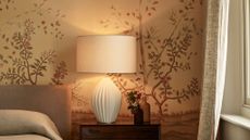 bedside ceramic lamp with cream base and shade, wooden bedside table and floral wallpaper