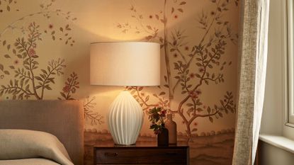 bedside ceramic lamp with cream base and shade, wooden bedside table and floral wallpaper