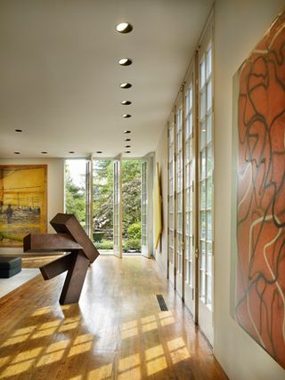 Image of a large room featuring a wooden sculpture and double open doors open behind it, with glass doors closed to the right