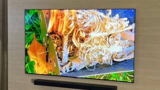 A wall-mounted LG G5 OLED TV displaying a pile of lit tinder