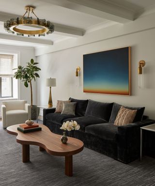 A living room with a statement gold light fixture, wavy wooden coffee table and dark gray velvet couch