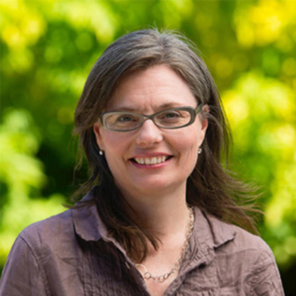 headshot of woman with brown hair, glasses and brown linen shirt