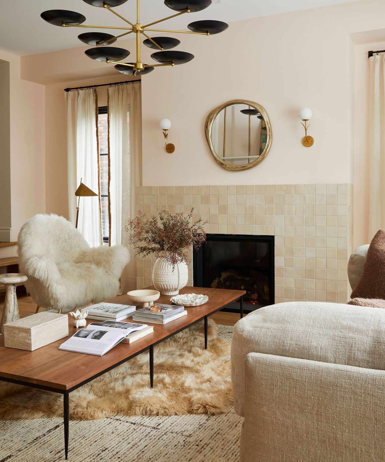A neutral living room with large black metal windows taking up one wall. There is a large beige sofa with a dog sitting on it and a tree to the left hand side. In front is a large wooden coffee table