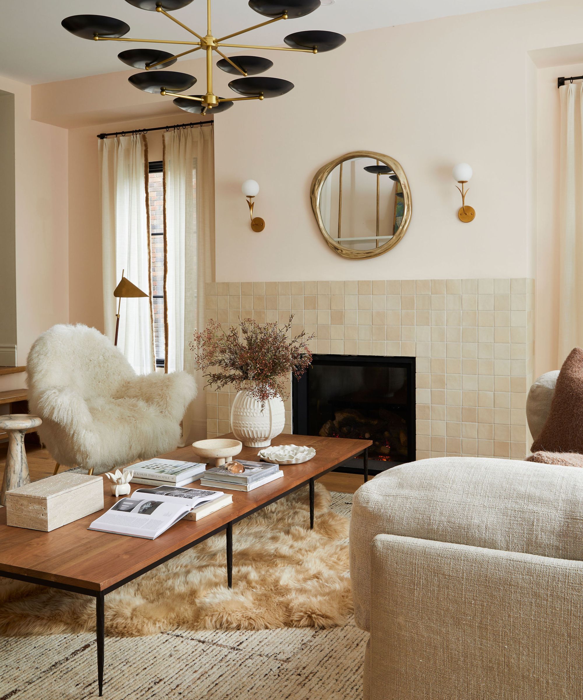 A neutral living room with large black metal windows taking up one wall. There is a large beige sofa with a dog sitting on it and a tree to the left hand side. In front is a large wooden coffee table