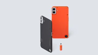 An orange CMF by Nothing Phone 1 standing on a white table with an extra black back plate and orange tool