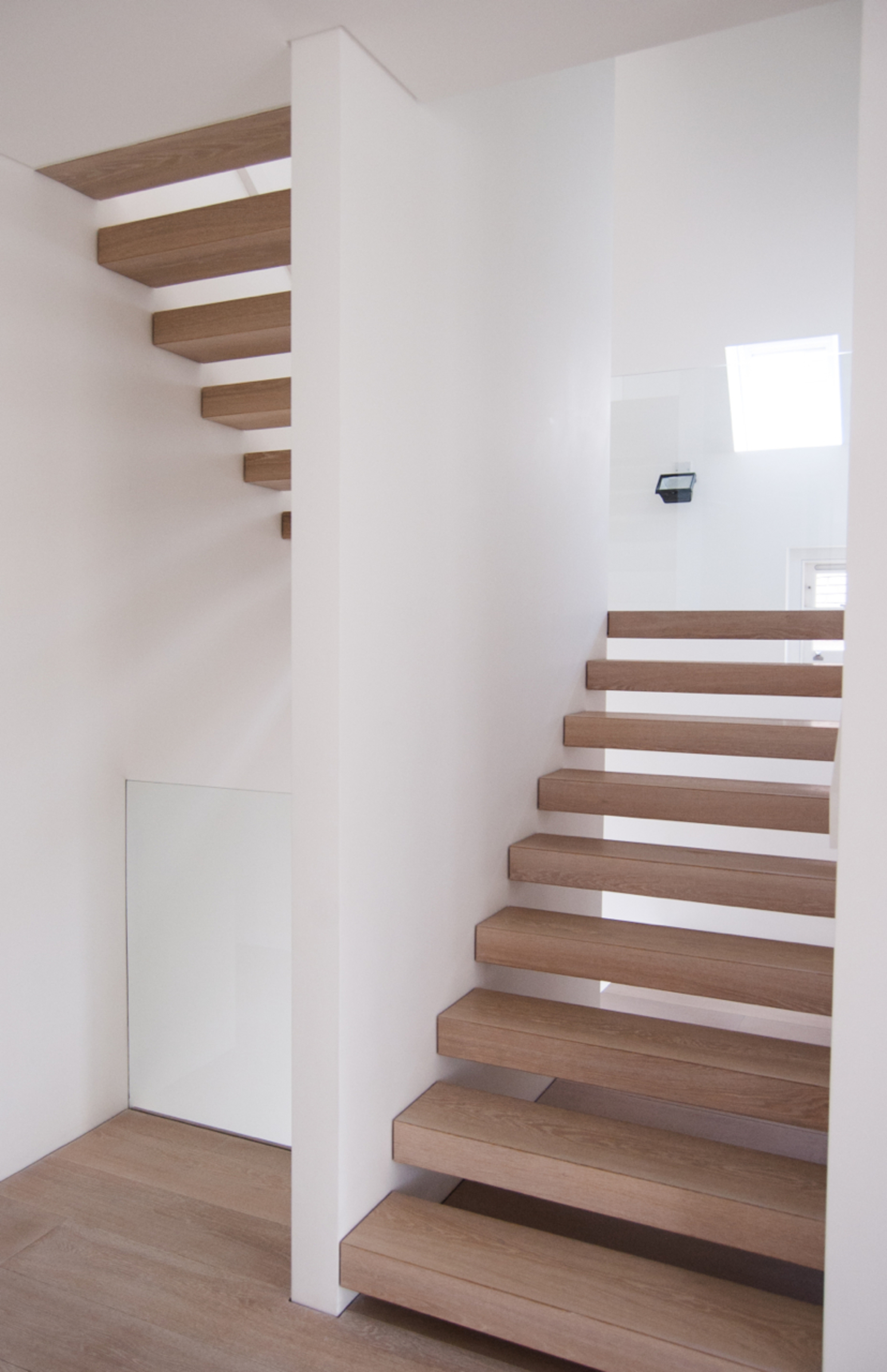 A set of wooden floating stairs leading to a loft space with a sky light